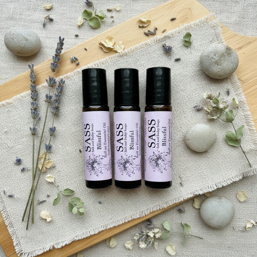 Three bottles of SASS Blissful roll-on essential oil on a wooden cutting board with lavender on the side and a couple rocks placed by