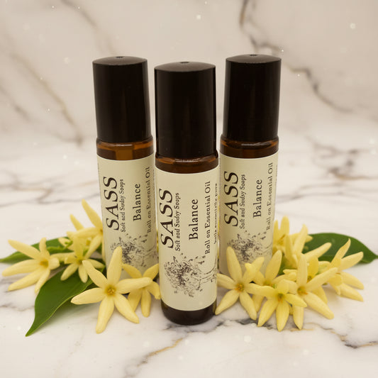 Three bottles of SASS Balance essential oil roll-ons on a marble background with ylang ylang 