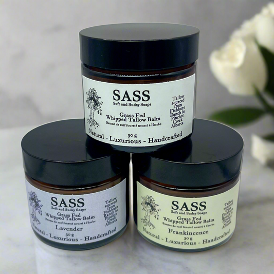 Three jars of SASS body balms on a marble surface with a blurred background