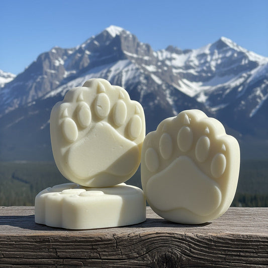 Three bear paw-shaped soap bars on a wooden surface with mountains in the background