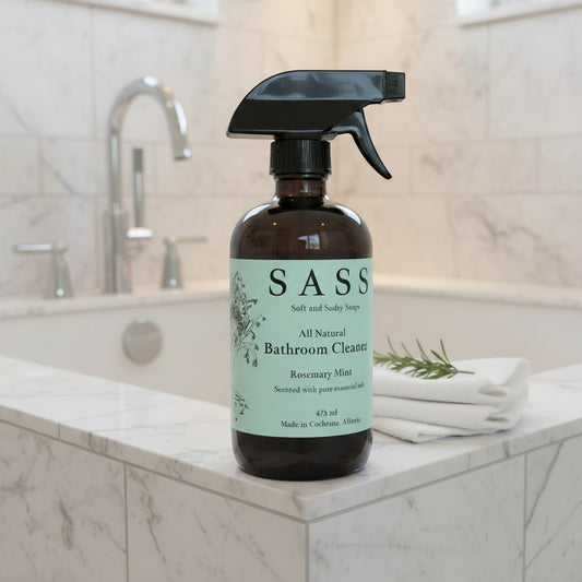 bottle of sass all natural bathroom cleaner sitting on tile tub with sprig of rosmary on folded white cloths