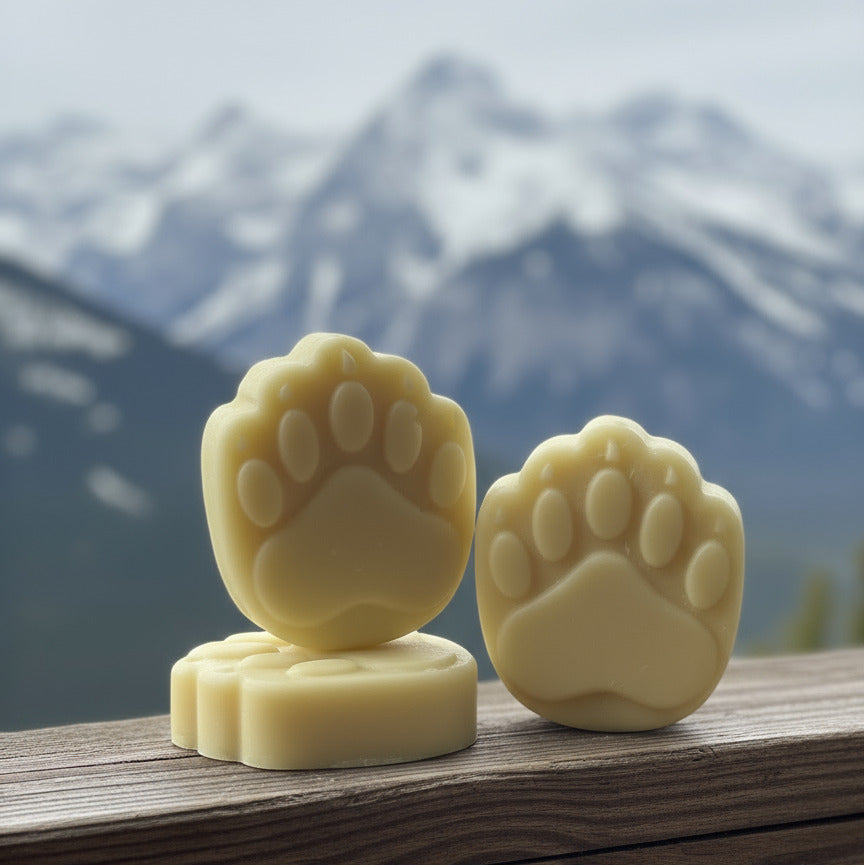 Two bear paw-shaped conditioner bars on a wooden ledge with a snowy canadian rocky mountain background 