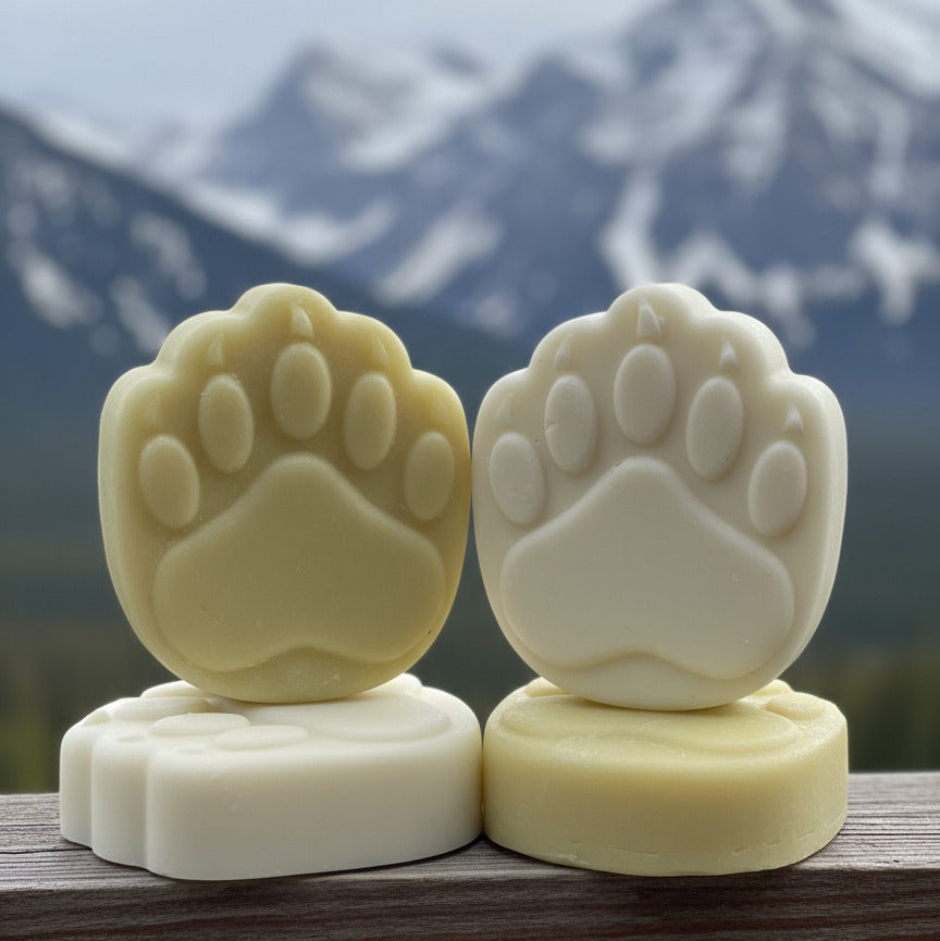 Two shampoo and conditioner bars shaped like bear footprints on a mountain background