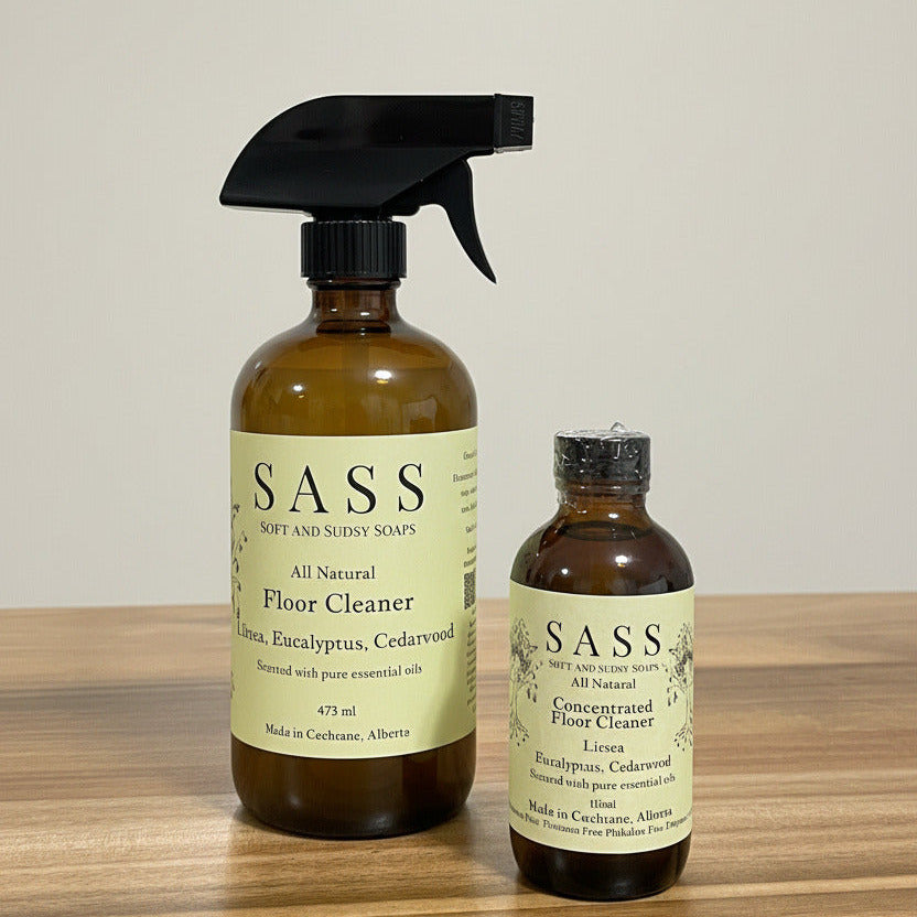 Two bottles of SASS all-natural floor cleaner on a wooden surface.