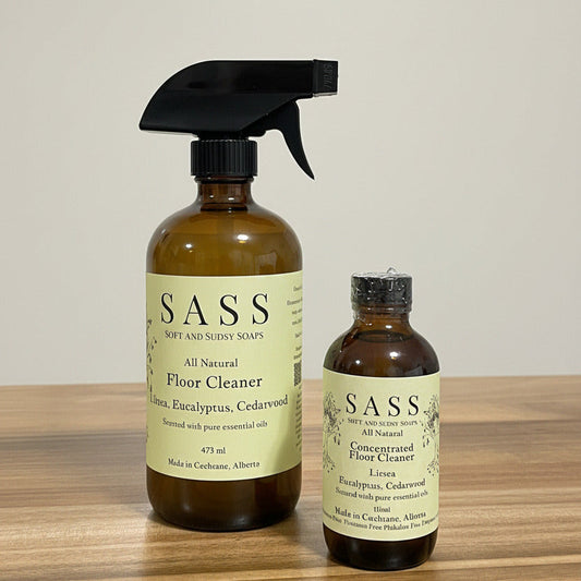 Two bottles of SASS all-natural floor cleaner on a wooden surface.