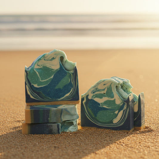 five bars of handcrafted soap with a swirled blue and green design, resembling ocean waves, on a beach background.